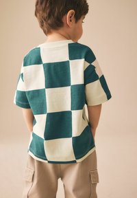 Zeleno-kremna karo bombažna majica s kratkimi rokavi in okroglim izrezom v kombinaciji s bež cargo hlačami.