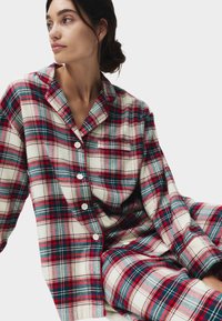 Set di pigiama a quadri rossi e verdi realizzato in tessuto morbido, composto da una camicia con bottoni e tasca e pantaloni larghi.