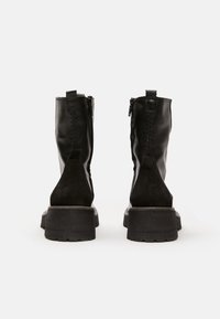 Botas de tobillo de cuero negro con un panel de ante, cremalleras laterales y una suela gruesa negra. Los detalles de costura en la parte posterior añaden textura.