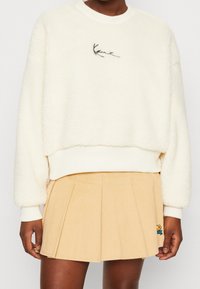 Krémová fleecová mikina s krátkým střihem a žebrovanými manžetami, doplněná béžovou plisovanou manšestrovou sukní s vyšívaným dekorem.