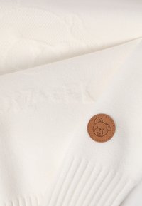 Pulover alb tricotat, cu un model texturat și o pată din piele maro cu un design de urs pe manșetă. Țesătură moale, ușoară.