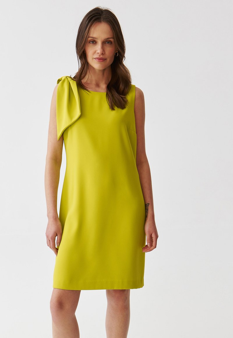 Vestido sin mangas de color amarillo con un detalle de lazo en un hombro, textura suave y un diseño simple de corte recto.