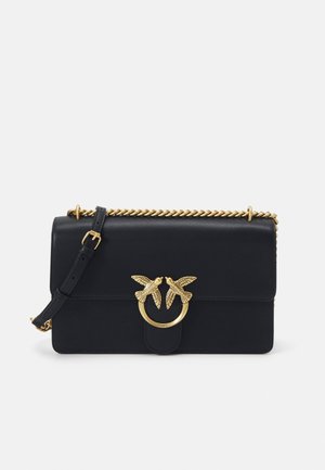 Črna usnjena torbica z zlatim verižnim trakom, okrasnim sistemom v obliki ptice, zložnim zapiranjem in gladko teksturo. Kompaktna pravokotna oblika.