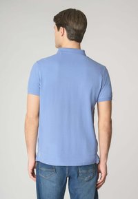 Polo shirt azzurro chiaro con una texture morbida, maniche corte e colletto. Presenta un orlo dritto con accenti sottili vicino alla cucitura laterale.
