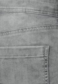 Vaaleanharmaa farkkukangas, jossa on takatasku näkyvillä ompeleilla ja sileällä pinnalla. Materiaali näyttää hieman haalistuneelta.