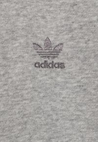Grått bomullstyg med en strukturerad yta, som har en mörkgrå broderad Adidas-logotyp med tre ränder och en treklöverdesign.