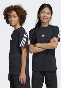 Camisetas de algodón negras con detalles de tres rayas blancas en las mangas. Una de las camisetas presenta un pequeño logo blanco en el pecho.