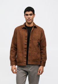 Pruun nööpidega jakk, millel on rinnatasku, kaks eesmist taskut ja tõmbluku detail. Puuvillane materjal pehme tekstuuriga.