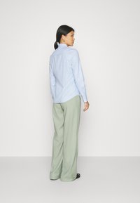 Hele helesinine nööbitav särk krae ja pikkade varrukatega, kehasse sobiv; sobitatud laia lõikega helesiniste pükstega ja mustade sandaalidega.