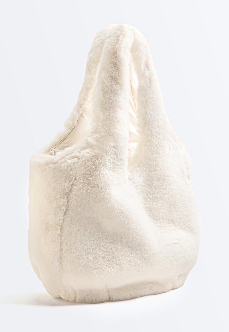 Sac cabas doux couleur crème en fausse fourrure avec une forme décontractée et de larges anses, photographié sur un fond blanc uni.