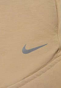 Beige szövet, kis szürke Nike swoosh logóval és látható varrással az alsó jobb sarokban.