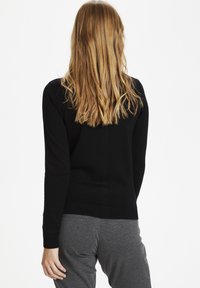 Black knit sweater with a fitted design, ribbed cuffs and hem. Worn with gray sweatpants, showing a smooth texture and clean lines.