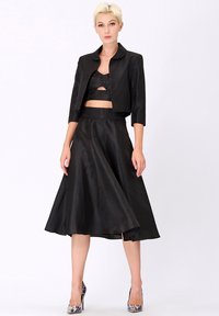 Ensemble noir en deux pièces comprenant une veste courte avec un col arrondi et une jupe fluide de longueur intermédiaire. Le tissu a une texture lisse.