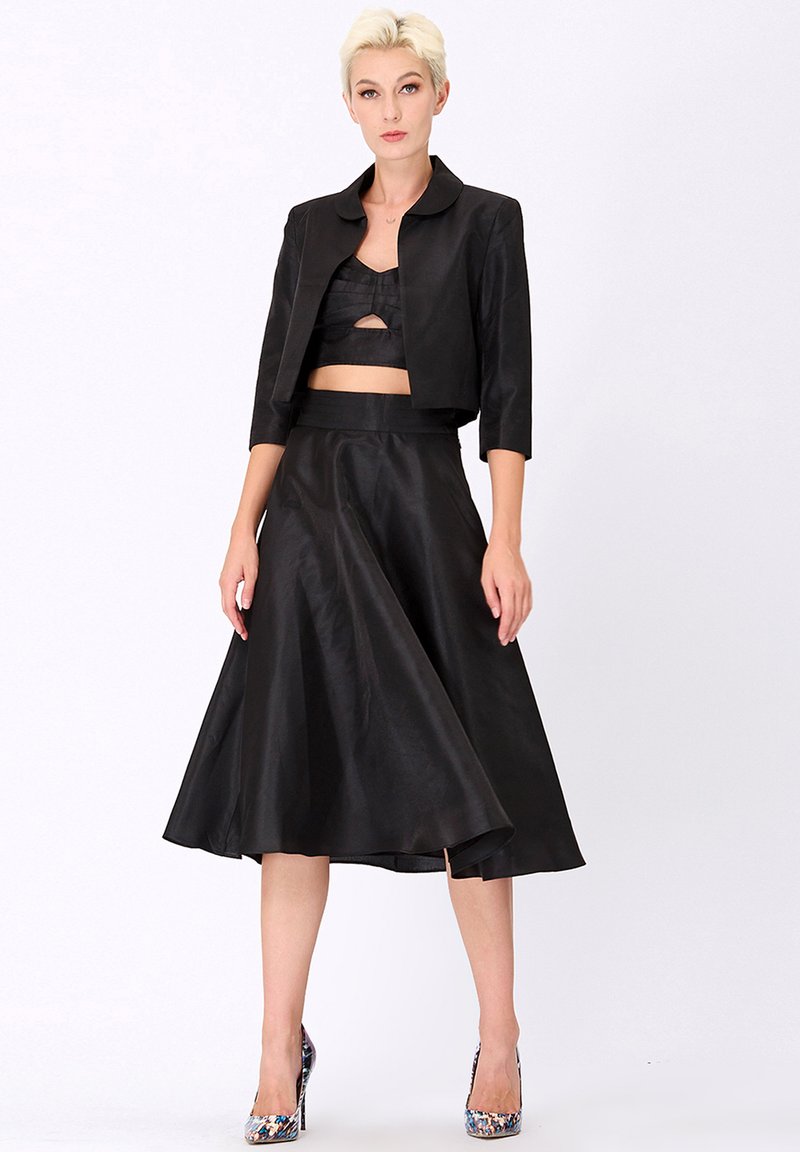 Ensemble noir en deux pièces comprenant une veste courte avec un col arrondi et une jupe fluide de longueur intermédiaire. Le tissu a une texture lisse.