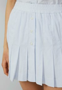 Lichtblauwe plissé rok met een gestreept patroon, elastische tailleband en vier decoratieve witte knopen aan de voorkant.