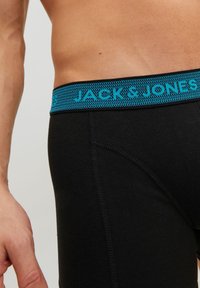 Schwarze Boxershorts mit einem blauen, gewebten Elastikbund, der den Text "JACK & JONES" zeigt. Merkmale sind eine glatte Textur und ein figurbetontes Design.