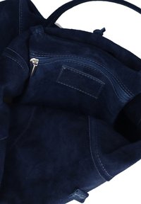Interno di una borsa in suede blu navy che mostra una tasca con zip e un tirazip in argento, con etichetta del marchio cucita all'interno.
