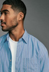 Button-up shirt with vertical blue and white stripes, lightweight fabric, and a patch pocket; worn over a white t-shirt.