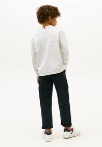 Grå sweatshirt med en vandret søm bagpå, parret med mørke cargo bukser med sidelommer og hvide sportssko med farveaccentuering.