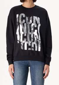 Sudadera negra con gráfico de texto plateado desgastado que dice "ICONIC." Cuenta con mangas largas y cuello redondo. El estilo es de corte relajado.
