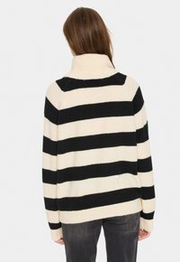 Cremfarbener und schwarzer gestreifter Pullover mit hohem Kragen, lockerer Passform und Stricktextur. Sichtbare Nähte an den Schultern und gerippte Bündchen.