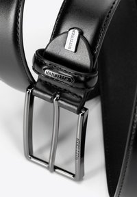 Zwarte leren riem met een metalen zilverkleurige gesp met rechthoekige punten. De gesp is gegraveerd met de merknaam "WITTCHEN."
