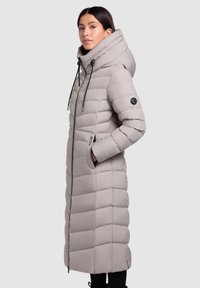 Manteau long gris rembourré avec un col haut, fermeture éclair, poches latérales et accents noirs. Présente un design matelassé pour l'isolation.