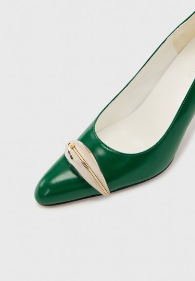 Πράσινο δερμάτινο γοβάκι με μυτερό μύτη και διακοσμητικό μεταλλικό κούμπωμα σε χρυσή απόχρωση στη μπροστινή πλευρά, παρουσιασμένο σε απλό φόντο.