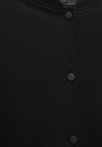 Schwarze Jacke mit glatter Textur, runder Kragen, Druckknopfverschluss und gerippten Akzenten am Hals.