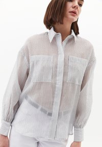 Langärmliges gestreiftes Hemd in Weiß und Schwarz mit einem Button-Down-Kragene sowie zwei Brusttaschen und einem transparenten, leichten Stoff.