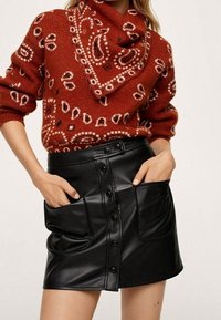 Rustykalny czerwony sweter z białymi wzorami paisley, zestawiony z czarną skórzaną mini spódnicą z dwiema przednimi kieszeniami i zapięciem na guziki.