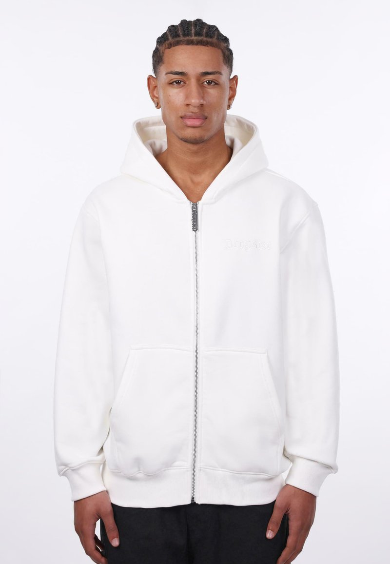 Haut à capuche blanc zippé en tissu doux, doté de poches avant, de poignets côtelés et d'une grande capuche. Présente un logo subtil sur la poitrine.