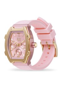 Montre en silicone rose avec un boîtier hexagonal doré, trois sous-cadrans et un bracelet texturé. Affiche le nom de la marque "ice watch."