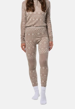 Femme portant un haut manches longues beige à motifs et des leggings assortis avec des chaussettes blanches, debout devant un fond uni.