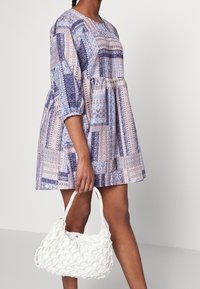 Sukienka w kwiatowy wzór w odcieniach niebieskiego i różowego, o luźnym kroju i rękawach do trzech czwarte. W komplecie z białą plecioną torebką.