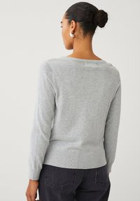 Lys grå sweater lavet af blød stof, med en bred halsudskæring og ribbede manchetter og kant, parret med mørke jeans.