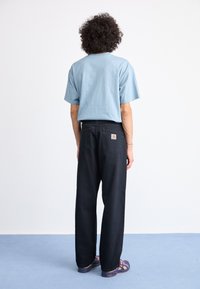Lyseblå kortærmet t-shirt med rund i halsen, parret med løstsiddende sorte bukser med baglommer og et logo-patch.
