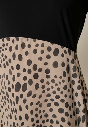 Schwarzes Oberteil trifft auf beigen Rock mit verstreuten schwarzen ovalen und runden Punkten in Spiralmustern auf glattem Stoff.