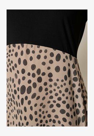 Sort top møder beige nederdel med spredte sorte ovale og runde pletter i spiral mønstre på glat stof.