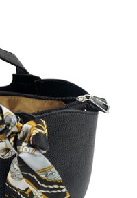 Zwarte leren emmer tas met een gestructureerd oppervlak, ritssluiting aan de bovenkant en een decoratieve gehaakte sjaal vastgebonden aan het handvat. Binnenkant is lichtbruin.