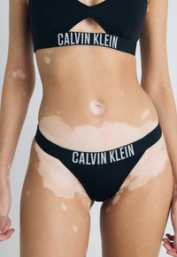 Czarny zestaw bielizny Calvin Klein składający si�ę z braletki i stringów, z logo na pasku, wycięciem i bezszwowym wykończeniem.