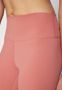 Høyt midje leggings i myk, elastisk stoff. Har en ensfarget støvete rosa farge med subtile sømmer langs sømmene.