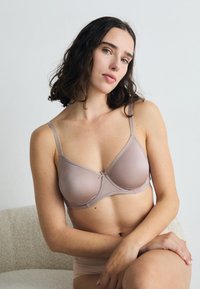 Light mauve bra with a smooth texture, underwire support, adjustable straps, and a central bow detail. Minimalistic design suitable for daily wear.