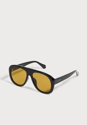 Gafas de sol con montura negra y grandes lentes tintadas de amarillo, inclinadas sobre fondo blanco, mostrando el logo "Prive Revaux" en la varilla.