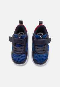 Baskets de sport bleu marine avec tissu en mesh, accents synthétiques gris, bande auto-agrippante, semelle blanche et détails rouges sur le talon.