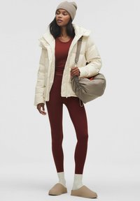 Puffjakke i creme med hætte, rød top der sidder tæt, matchende leggings, beige slip-on sko og en slasket grå taske. Blød tekstur hele vejen igennem.