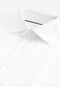 Camisa blanca de algodón con cuello clásico, presenta tres botones y una textura tejida. Etiqueta visible dentro del cuello.