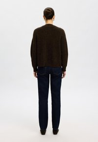 Barna kötött pulóver laza szabással, sötétkék egyenes szárú farmernadrággal párosítva. Egyszínű textúra, rövidített hossz, és minimális dizájnelemek.