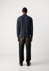 Navy blue knitted cardigan with a relaxed fit, long sleeves, and a collar, paired with black loose-fitting trousers and black shoes.