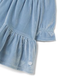 Abbigliamento in velluto blu chiaro con orlo arricciato, caratterizzato da una texture morbida, una cucitura decorativa sulla manica e un piccolo dettaglio a bottone.